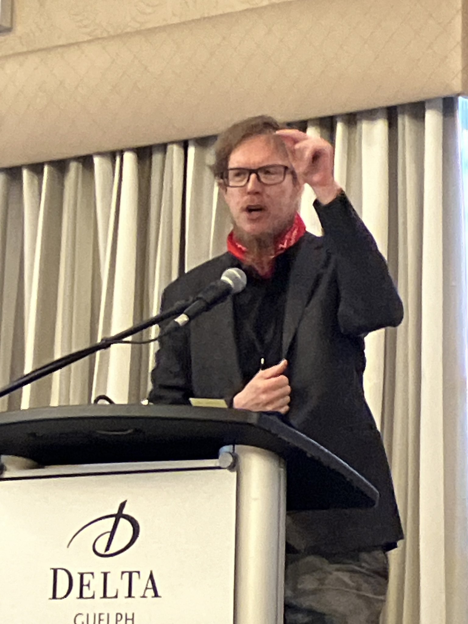 Jesse Hirsh qui parle à un pupitre d'un hôtel Delta.
