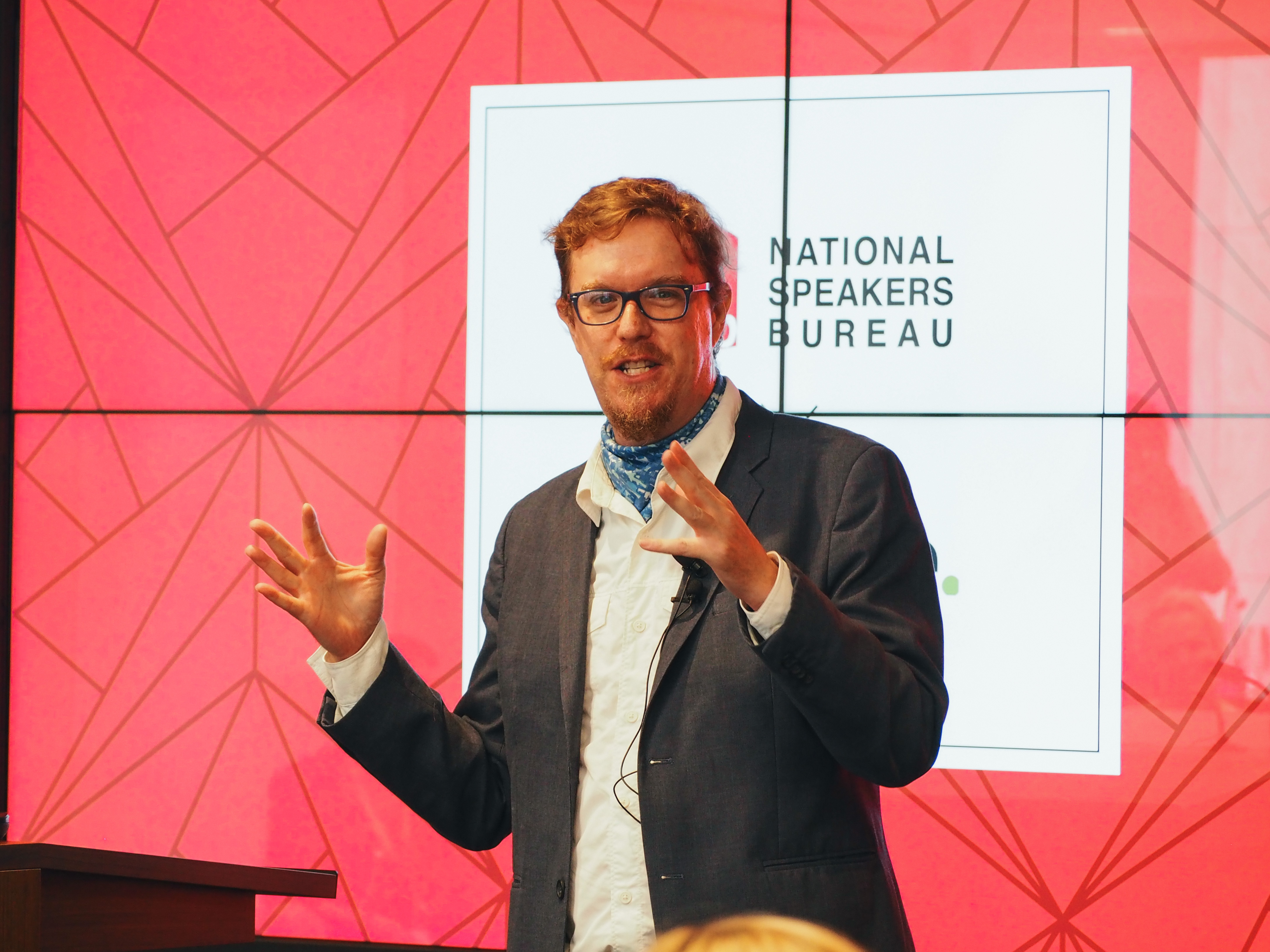 Jesse Hirsh qui parle à un pupitre devant un écran du National Speakers Bureau.