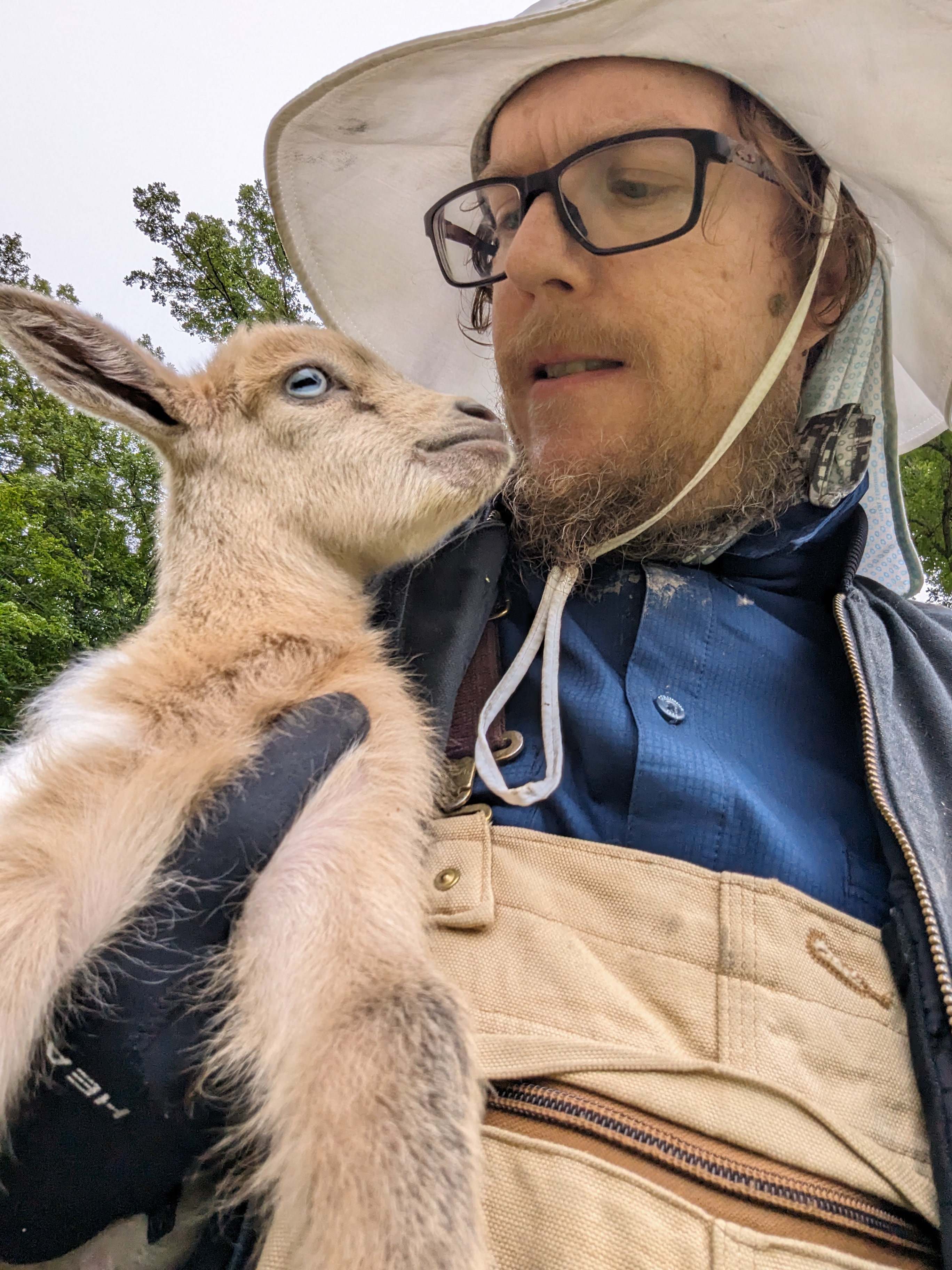 Jesse Hirsh sosteniendo un cabrito cerca de su rostro al aire libre.